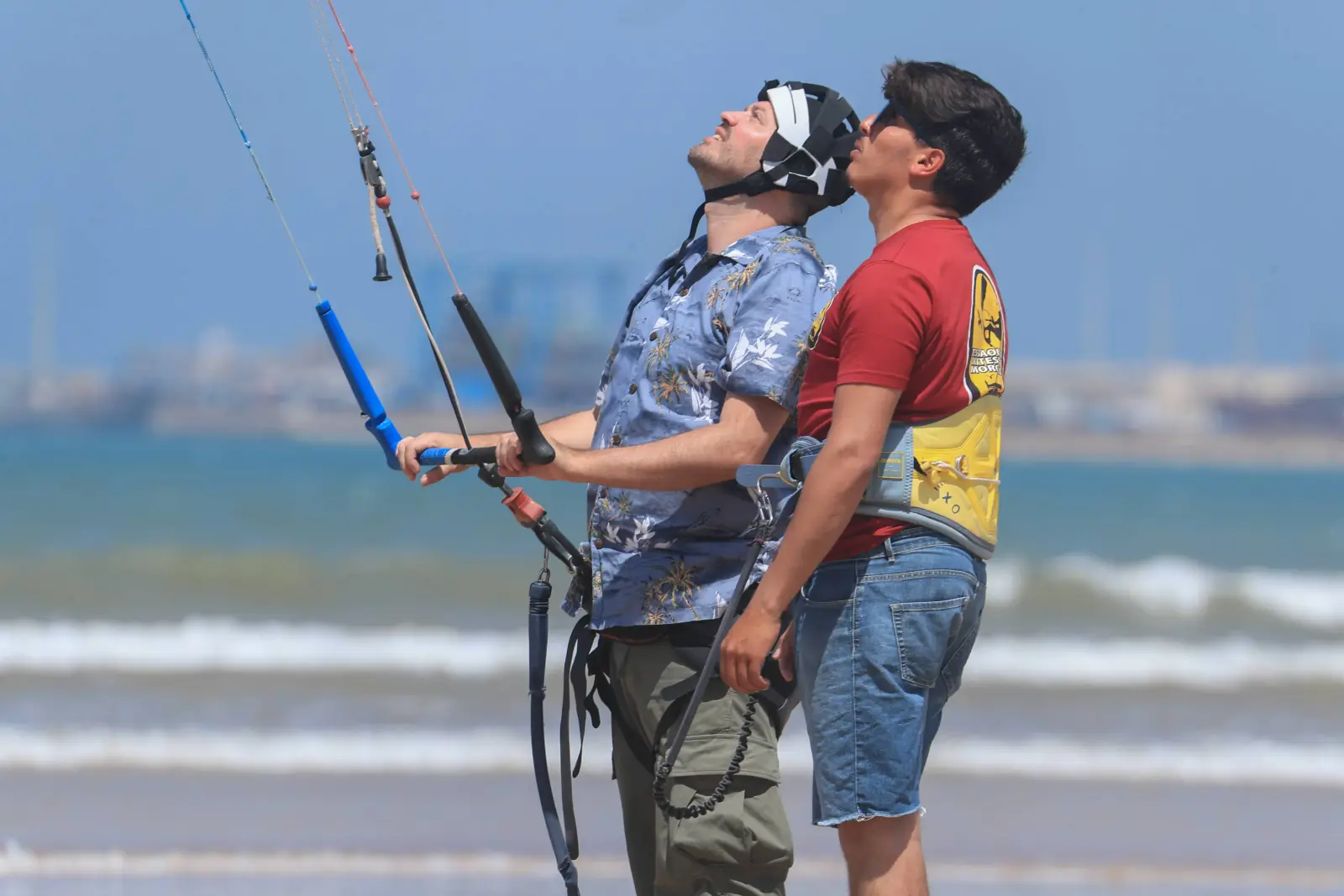 Deux personnes sur la plage regardent l'aile au-dessus d'elles ; l'une tient la barre de pilotage, l'autre se tient juste derrière.