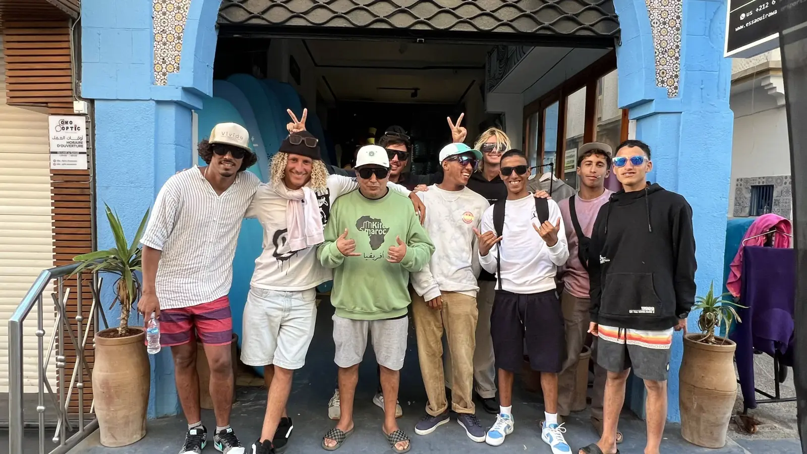 A group of people smiling and making hand gestures in front of a shop with a bright blue painted entrance.